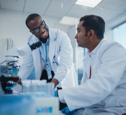 two scientists in lab smiling and talking over microscope