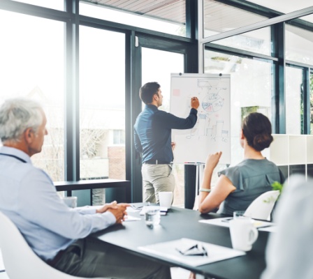 several employees in meeting room while businessman writes stats on notepad